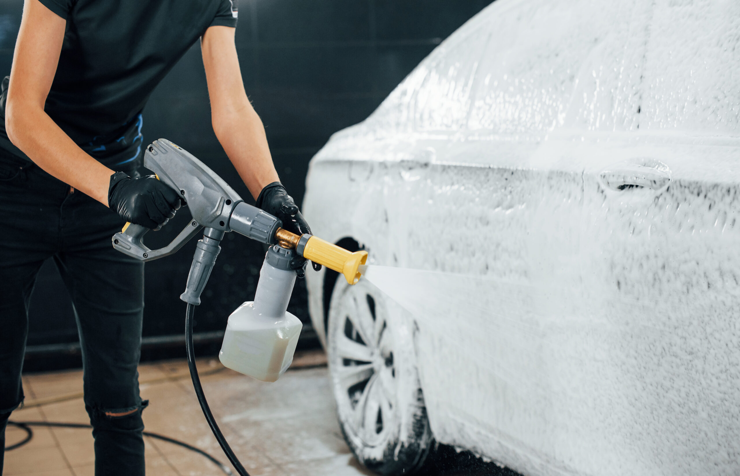 Using high pressure water. Modern black automobile get cleaned by woman inside of car wash station